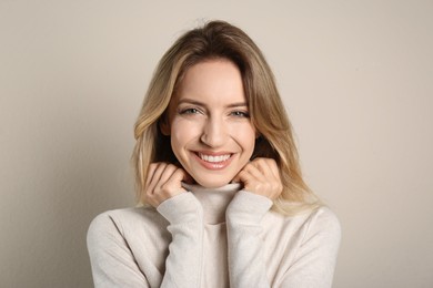 Portrait of happy young woman with beautiful blonde hair and charming smile on beige background