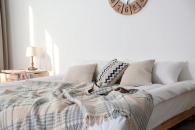 Bed with pillows and plaid near light wall. Cozy interior design