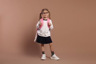 Photo of Happy schoolgirl in glasses with backpack on brown background