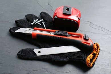 Photo of Utility knife, measuring tape and glove on black table, closeup