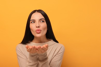 Beautiful young woman blowing kiss on orange background. Space for text