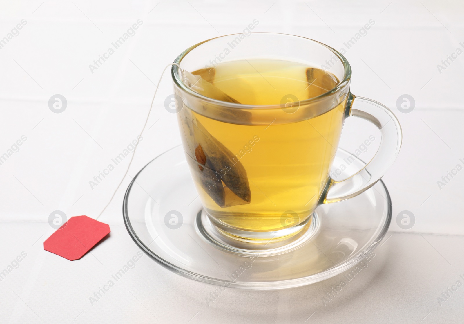 Photo of Tea bag in cup with hot drink on white table, closeup