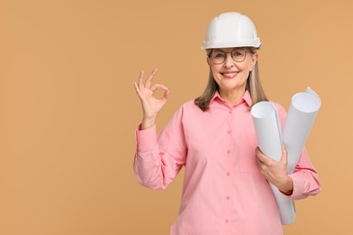 Photo of Architect in hard hat with drafts showing ok gesture on beige background, space for text