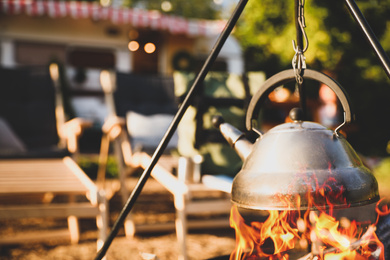 Image of Teapot heating on open fire outdoors. Camping season