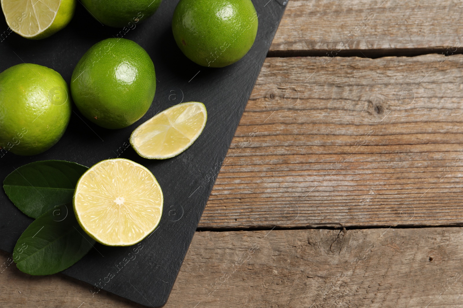 Photo of Fresh limes and green leaves on wooden table, top view. Space for text