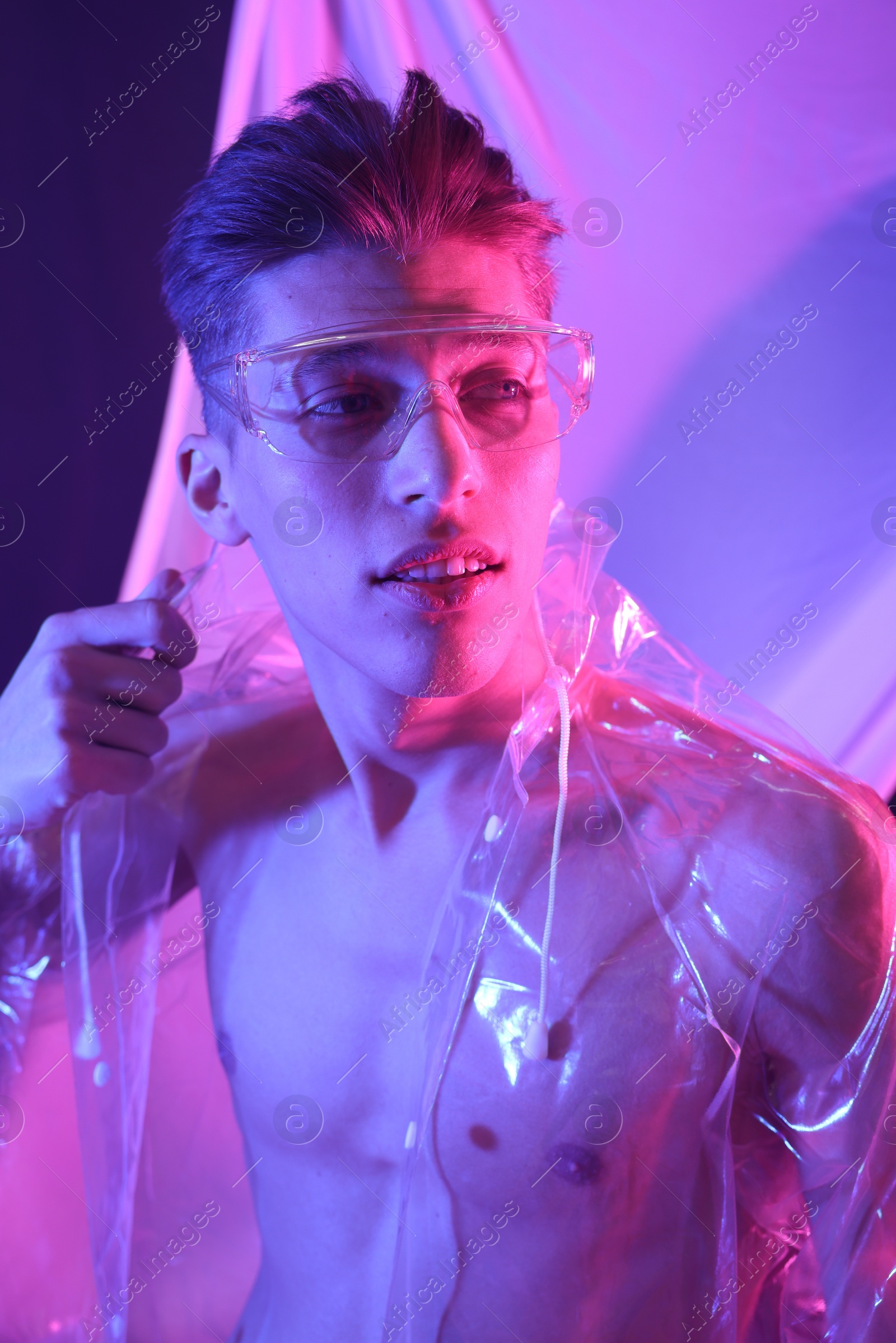 Photo of Stylish young man wearing clear coat and glasses in neon lights