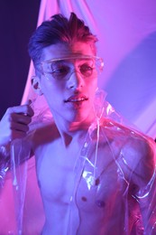 Stylish young man wearing clear coat and glasses in neon lights