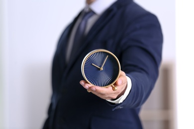 Businessman holding alarm clock on blurred background. Time concept