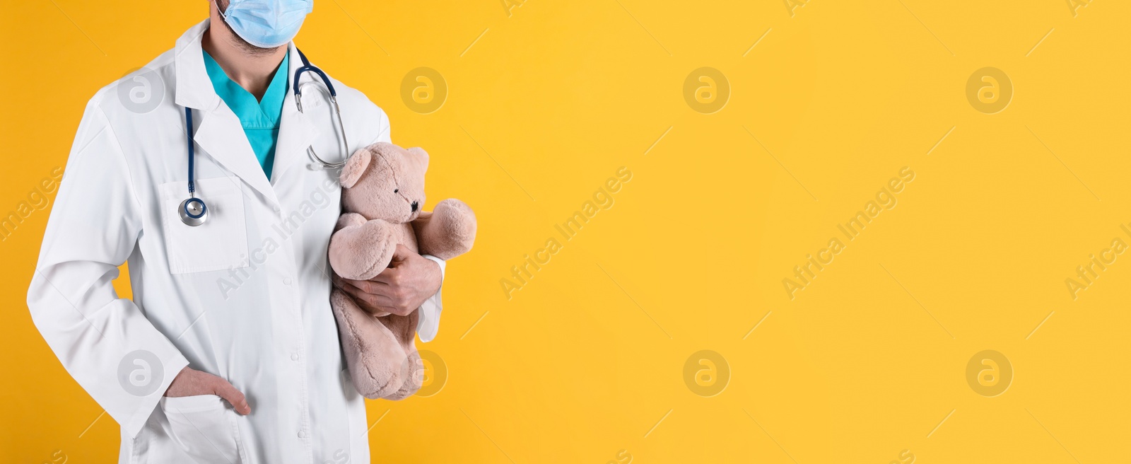 Photo of Pediatrician with teddy bear and stethoscope on yellow background, closeup. Space for text