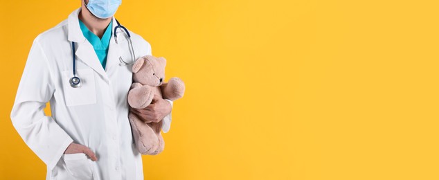 Photo of Pediatrician with teddy bear and stethoscope on yellow background, closeup. Space for text