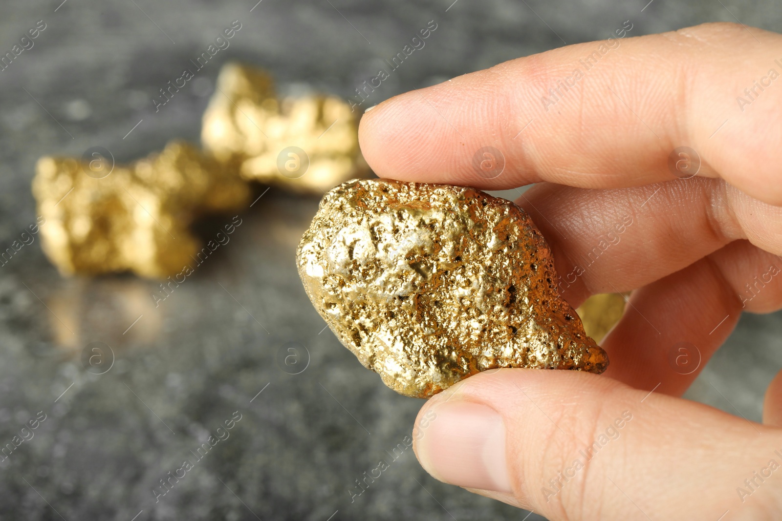 Photo of Woman holding gold nugget at grey textured table, closeup. Space for text