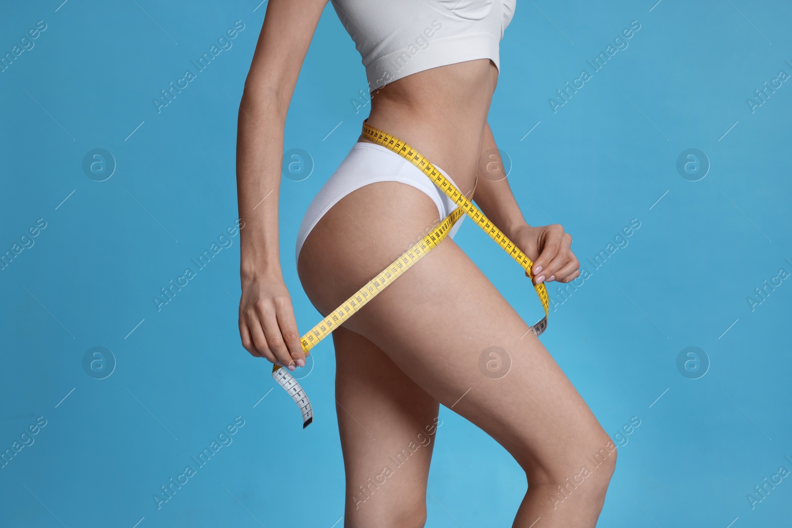Photo of Young woman measuring waist with tape on light blue background, closeup