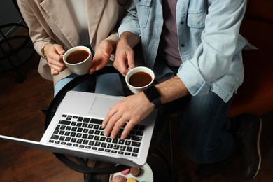 Photo of Couple with coffee and laptop spending time together in cafe, above view