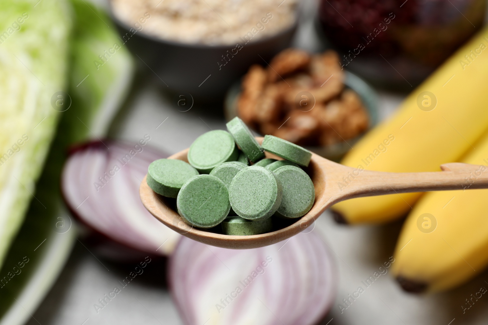 Photo of Wooden spoon of pills over table with foodstuff, closeup. Prebiotic supplements