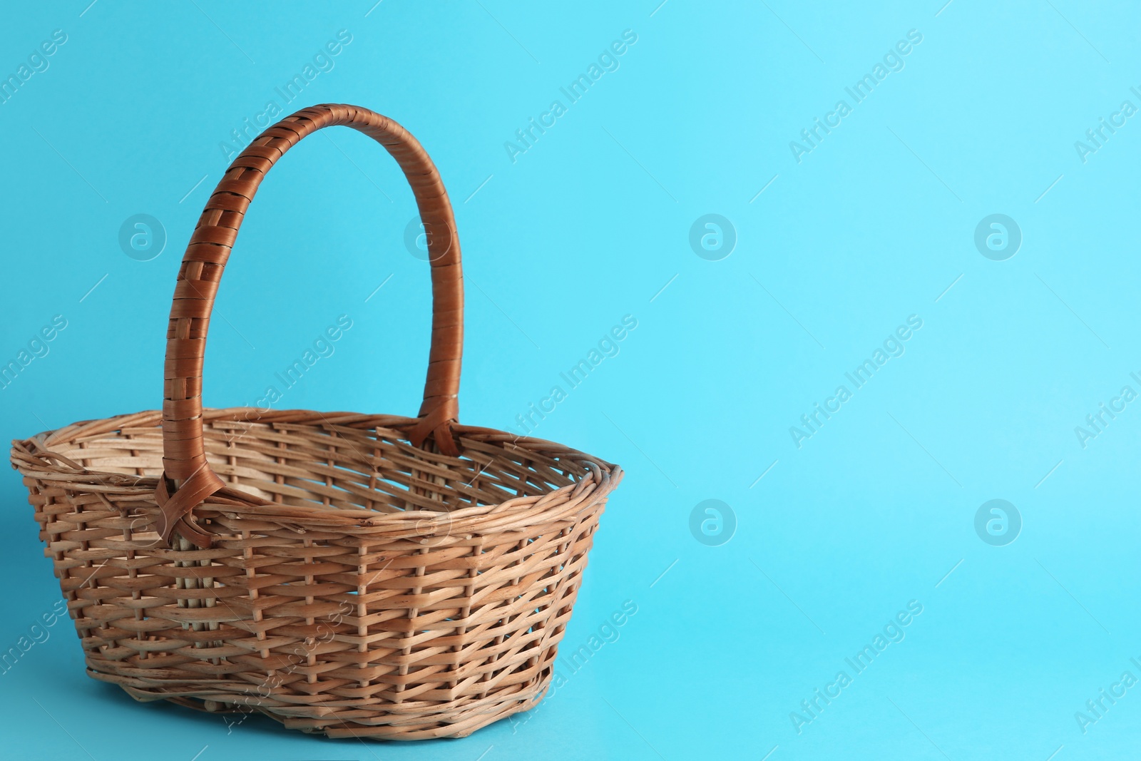 Photo of Empty wicker basket on light blue background, space for text. Easter item