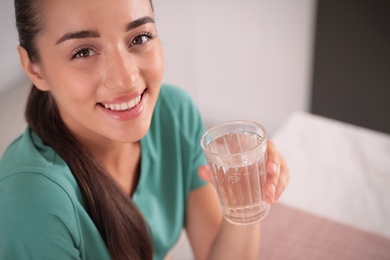 Photo of Young woman holding glass of pure water indoors, closeup