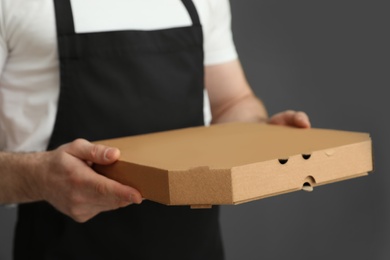 Waiter in apron with pizza box on grey background, closeup. Food delivery service