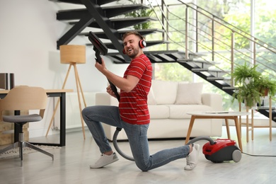 Young man having fun while vacuuming in living room