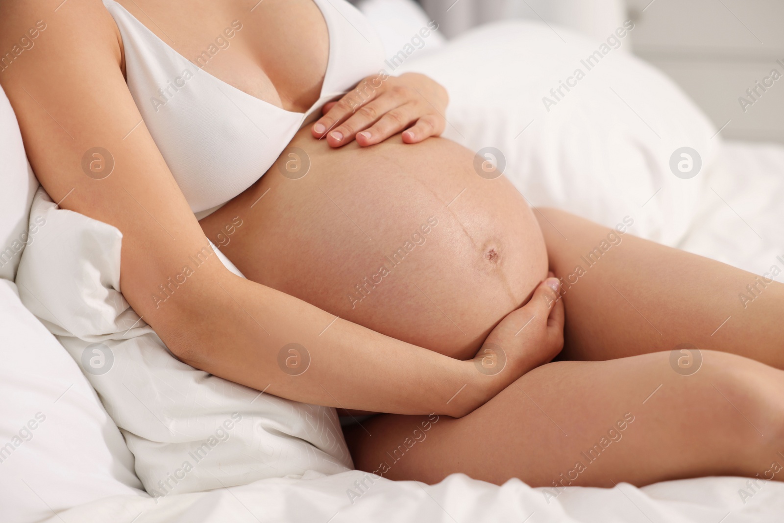 Photo of Pregnant woman in stylish comfortable underwear on bed indoors, closeup