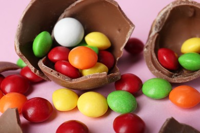 Photo of Broken chocolate egg with colorful candies on pink background, closeup