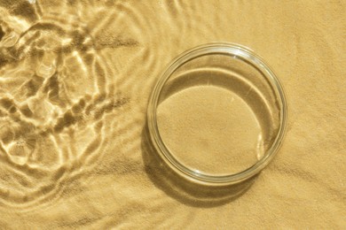 Photo of Stylish presentation for product. Glass podium in water on sand, top view. Space for text