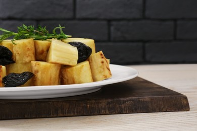 Tasty homemade parsnips with prunes and rosemary on white wooden table, closeup. Space for text