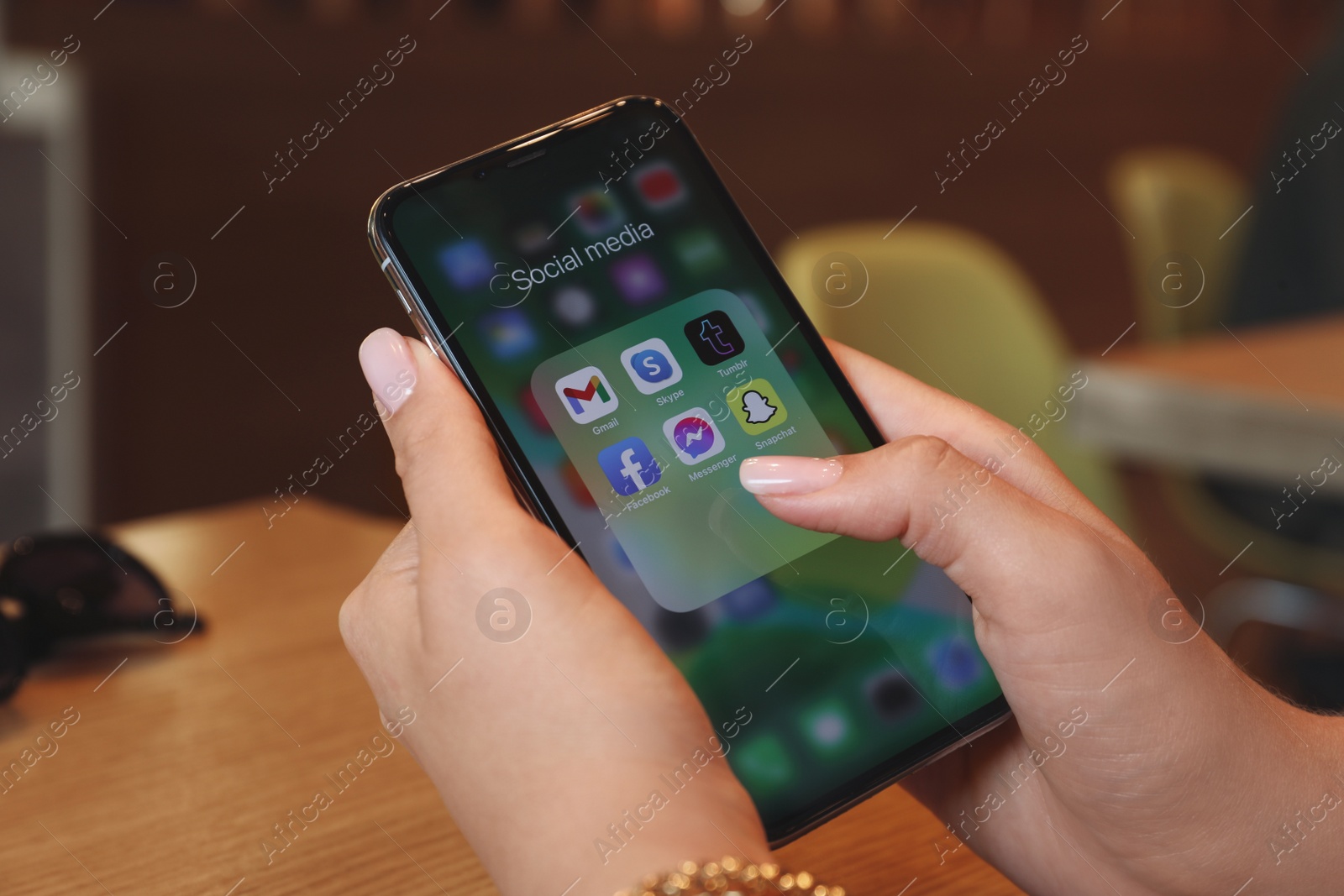 Photo of MYKOLAIV, UKRAINE - AUGUST 11, 2021: Woman using Apple iPhone X at wooden table, closeup. Screen with different social media icons