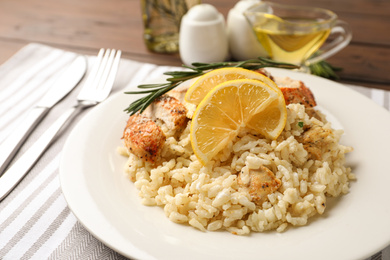 Photo of Delicious chicken risotto with lemon slices on table