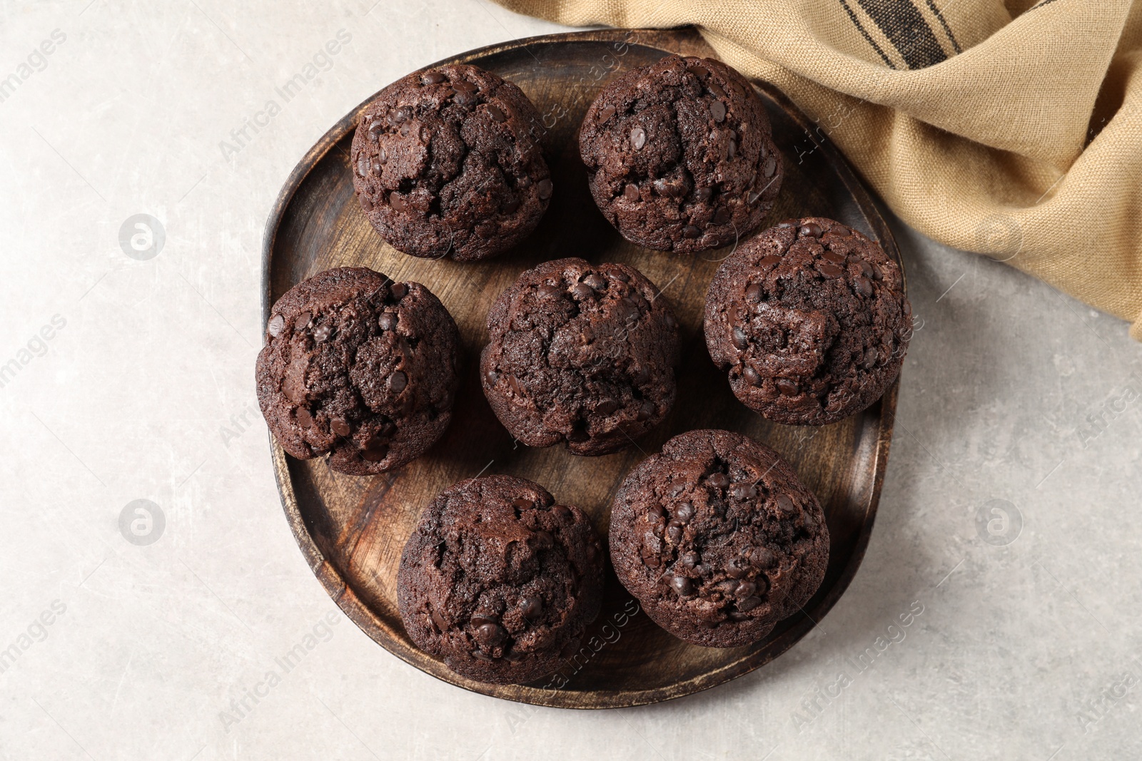 Photo of Board with delicious chocolate muffins on light table, top view