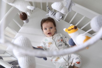 Cute little baby looking at hanging mobile in crib, top view