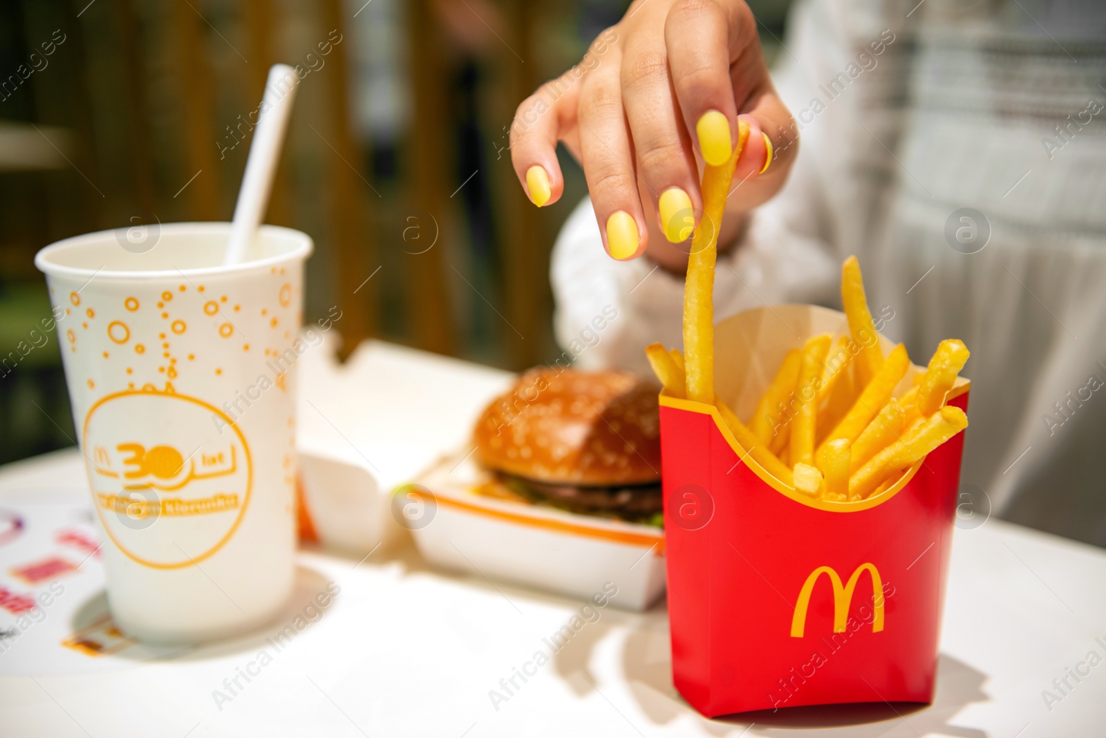 Photo of WARSAW, POLAND - SEPTEMBER 04, 2022: Woman with McDonald's French fries, burger and drink at table in cafe, closeup