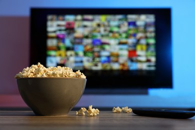 Photo of Bowl of popcorn and TV remote control on table indoors