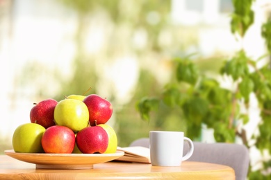 Photo of Plate with different sweet apples and cup of coffee on table in room