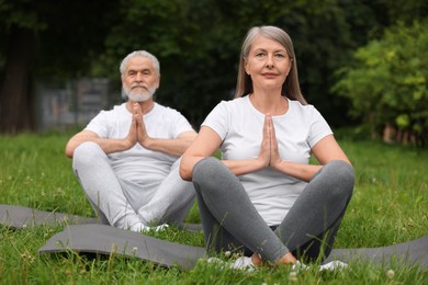 Photo of Senior couple practicing yoga on green grass in park, selective focus
