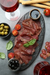 Delicious bresaola, wine and different products served on grey textured table, flat lay