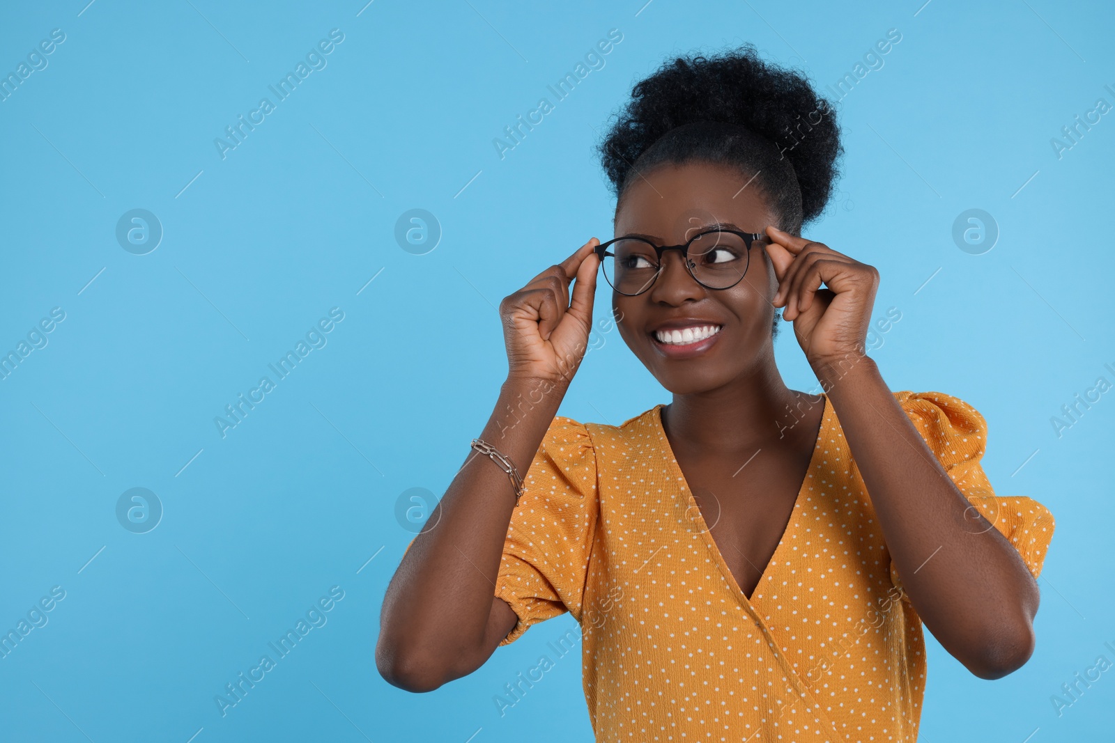 Photo of Portrait of beautiful young woman in eyeglasses on light blue background, space for text