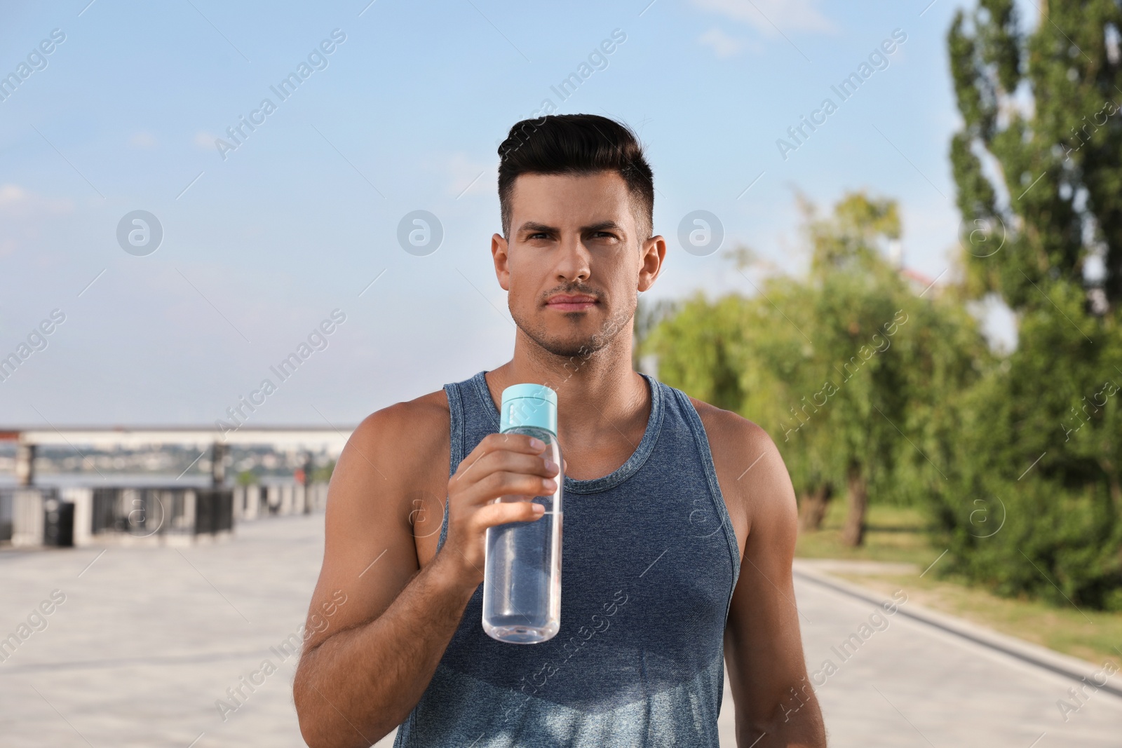 Photo of Handsome man in sportswear with bottle of water outdoors on sunny day