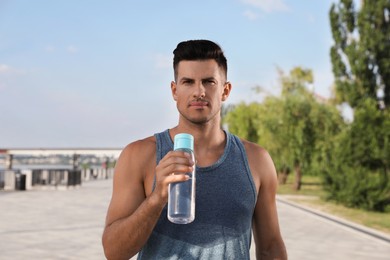 Handsome man in sportswear with bottle of water outdoors on sunny day