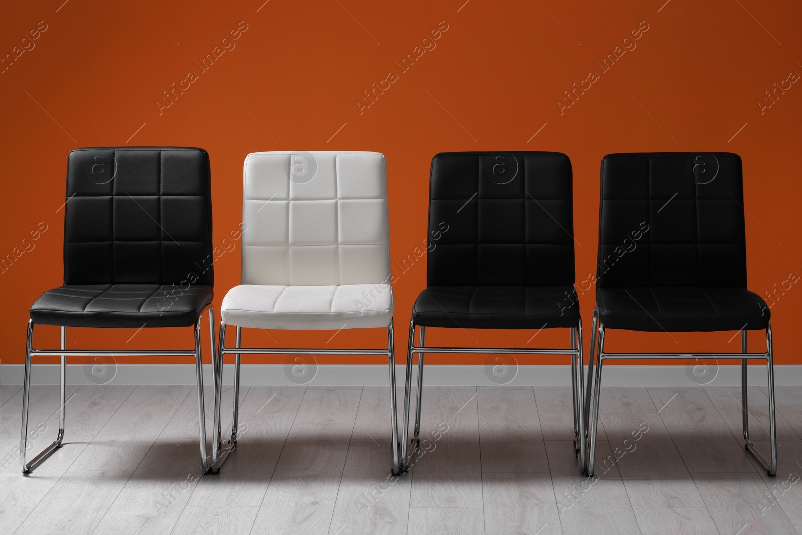 Photo of Black chairs with white one near orange wall. Recruiter searching employee