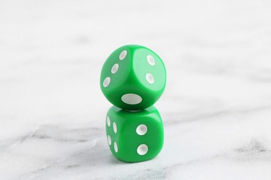 Two green game dices on white marble table, closeup