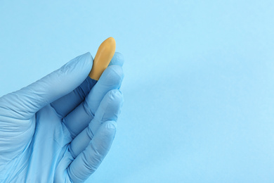 Photo of Closeup view of woman holding suppository on light blue background, space for text. Hemorrhoid treatment