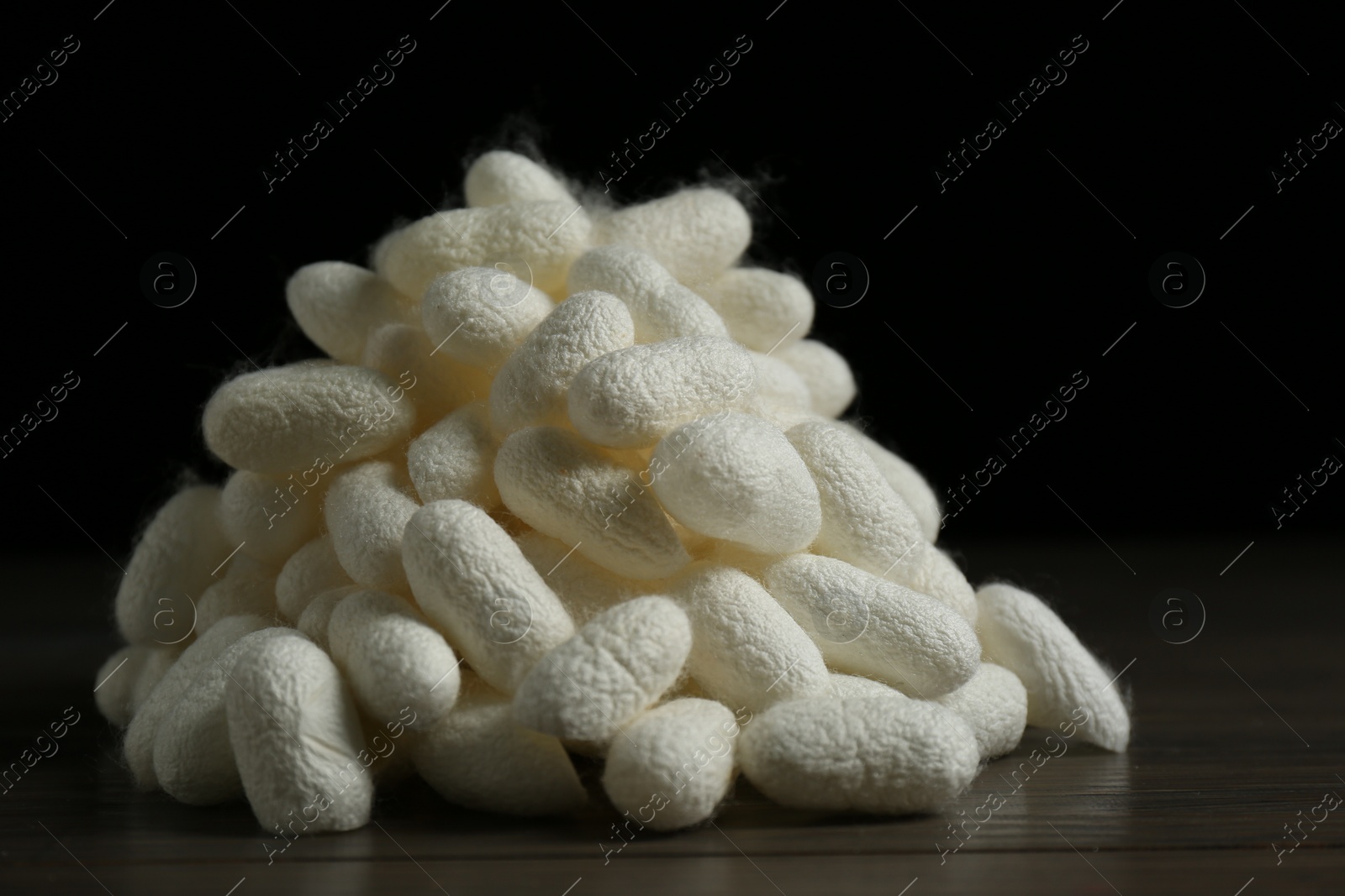 Photo of Heap of white silk cocoons on wooden table, closeup