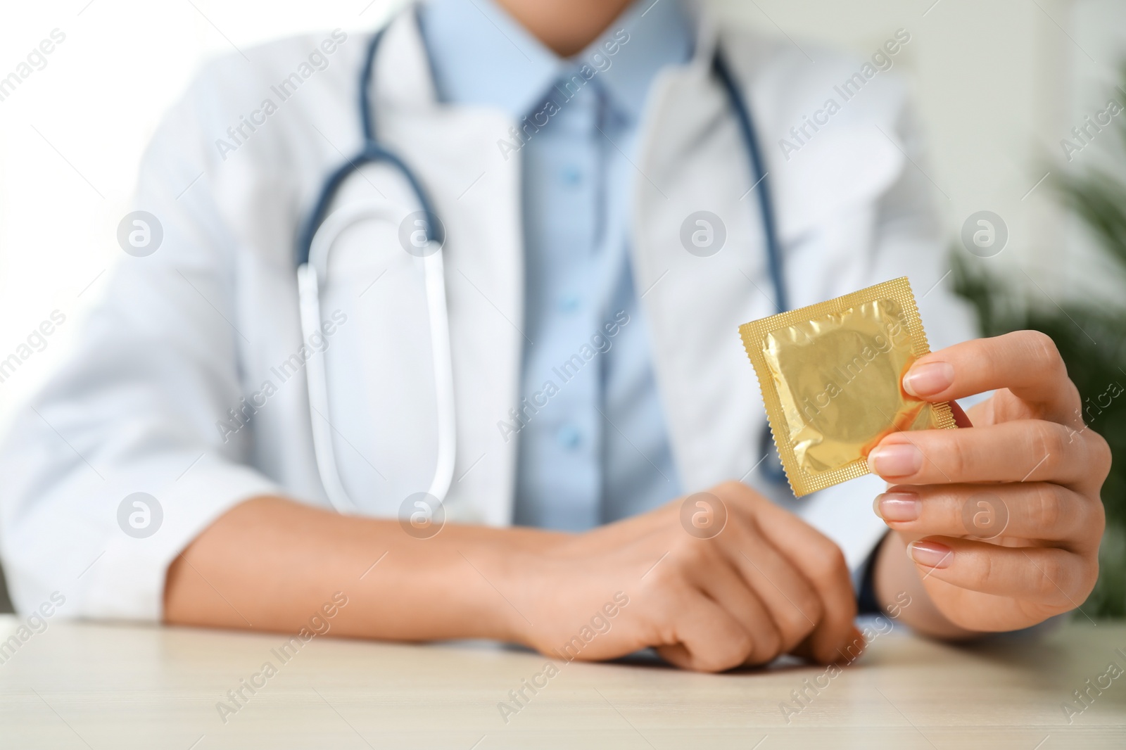 Photo of Female doctor holding condom at table indoors, closeup. Safe sex concept