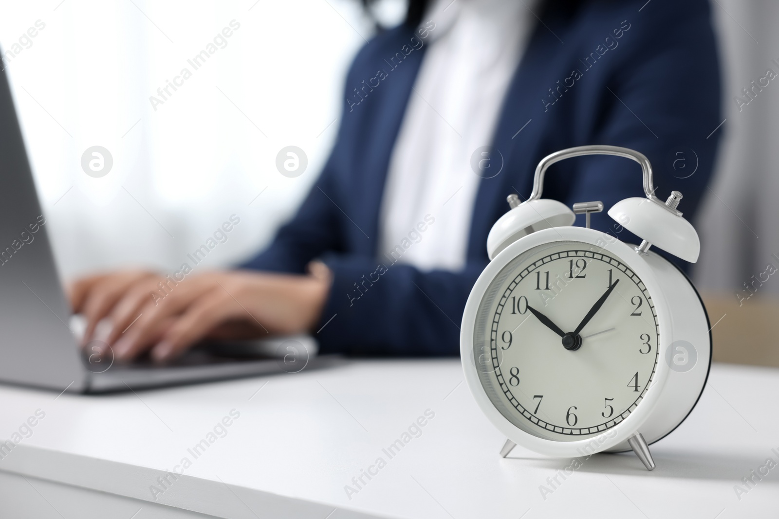 Photo of Stressful deadline. Alarm clock near woman working at white desk indoors, closeup. Space for text