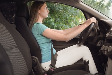 Young woman with fastened safety belt on driver's seat in car