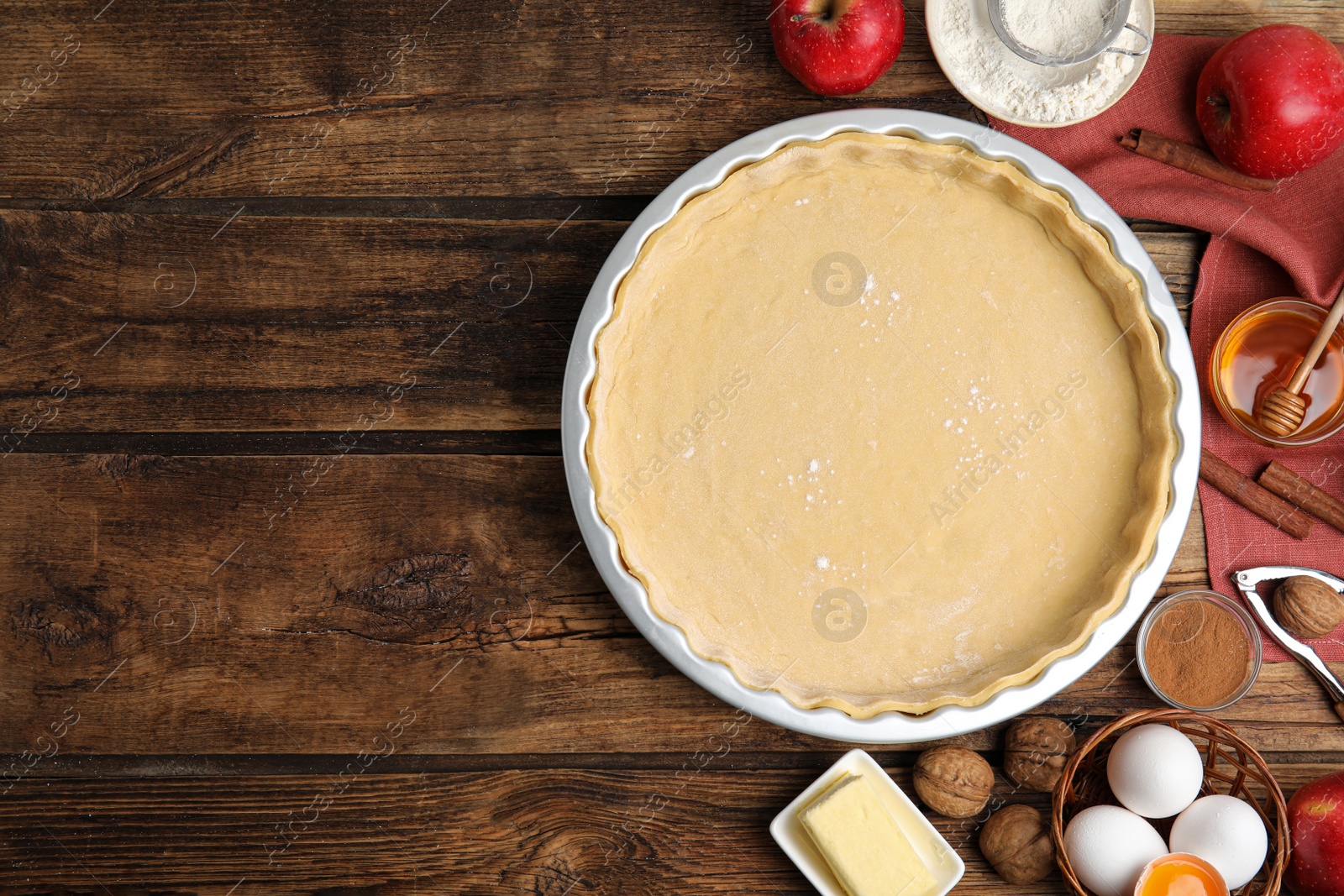 Photo of Raw dough and traditional English apple pie ingredients on wooden table, flat lay. Space for text