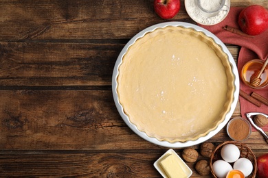 Raw dough and traditional English apple pie ingredients on wooden table, flat lay. Space for text