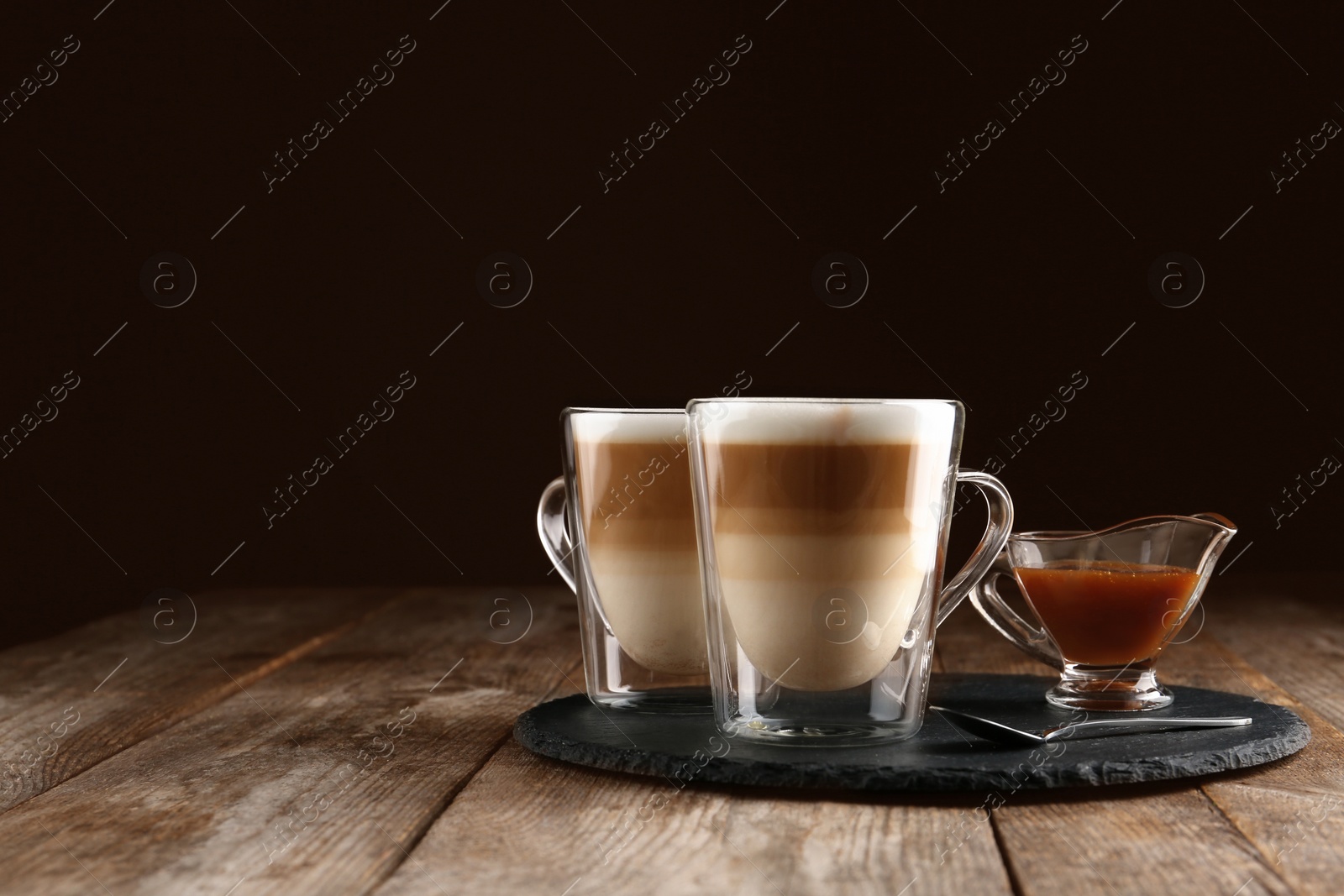Photo of Glass cups of caramel macchiato and gravy boat with syrup served on table, space for text