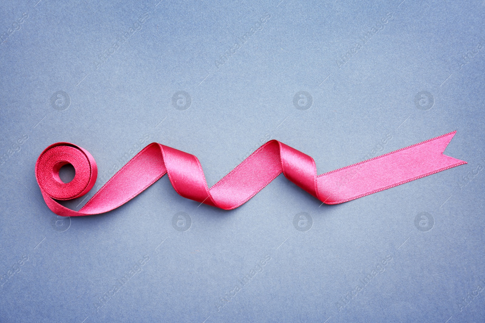 Photo of Simple pink ribbon on color background, top view