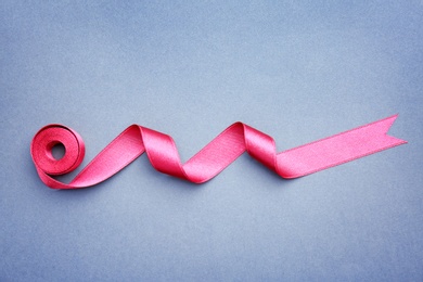 Photo of Simple pink ribbon on color background, top view